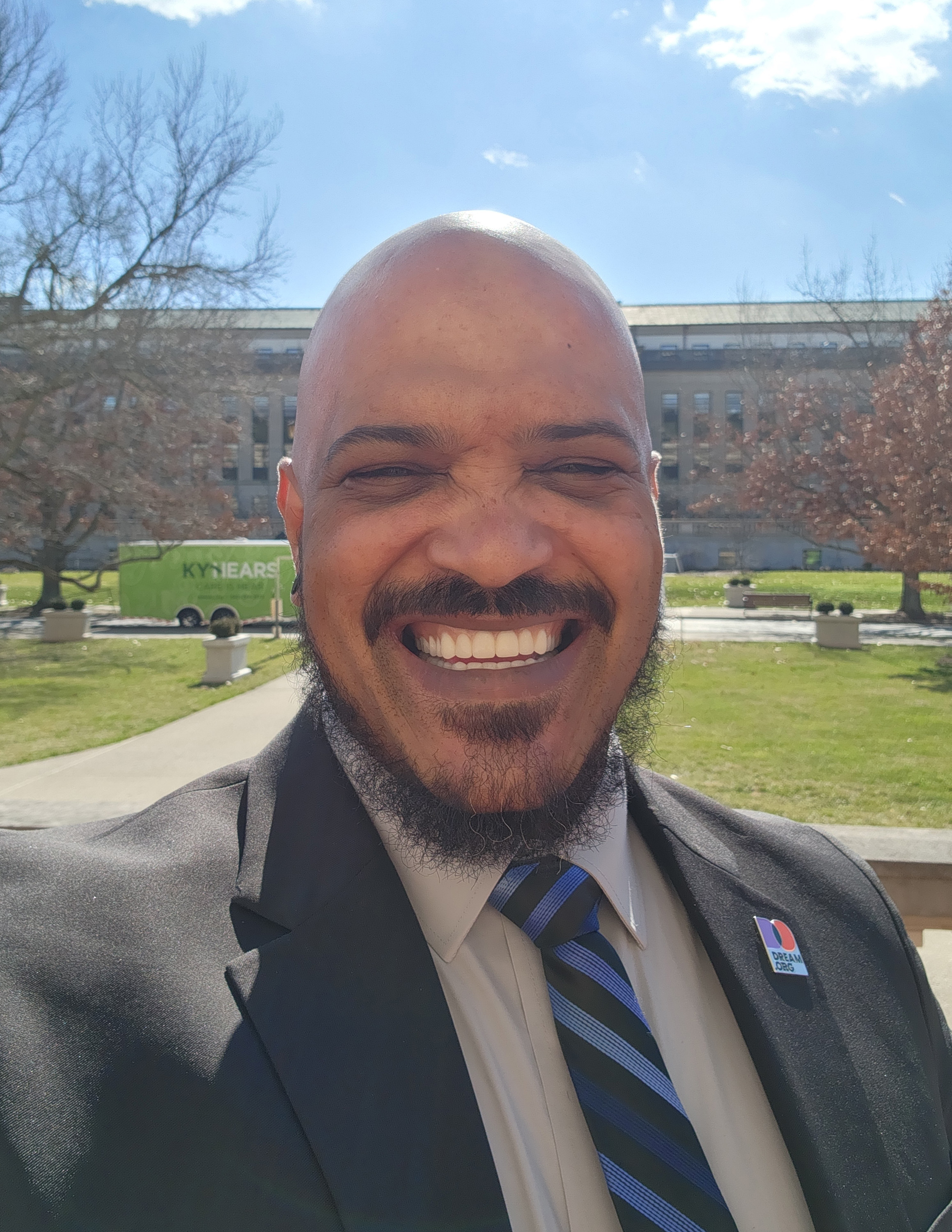 A photo of a black man smiling for a photo outside.